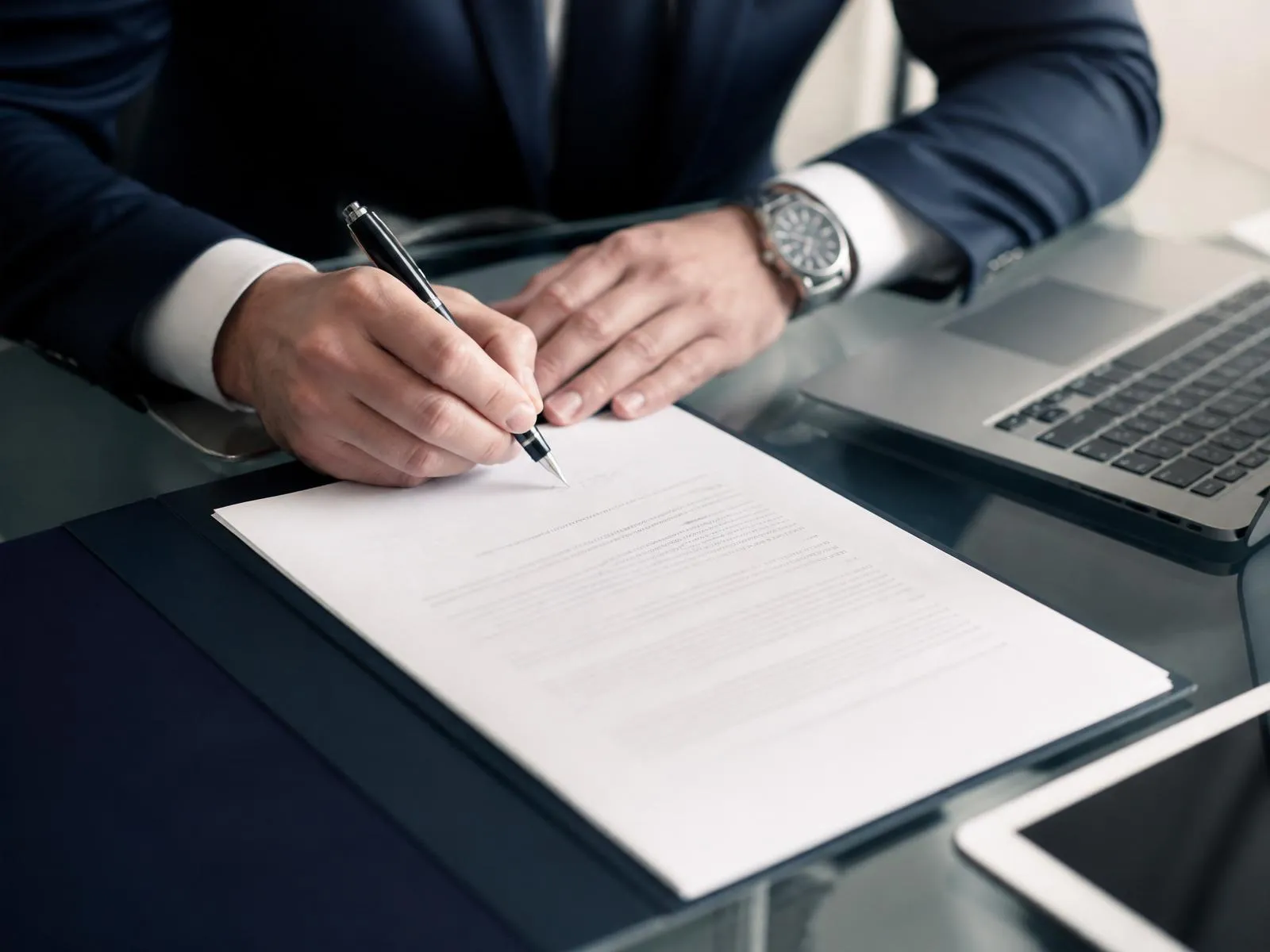 Ejecutivo firmando documento con laptop y tablet